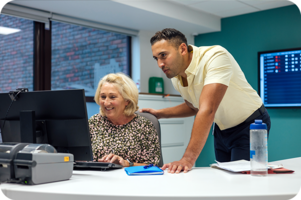 ARRS-funded clinical pharmacist supporting a GP practice staff member at a computer in a primary care network office