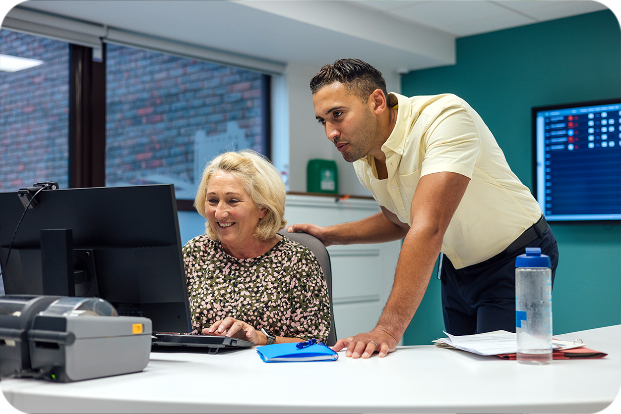 ARRS-funded clinical pharmacist supporting a GP practice staff member at a computer in a primary care network office